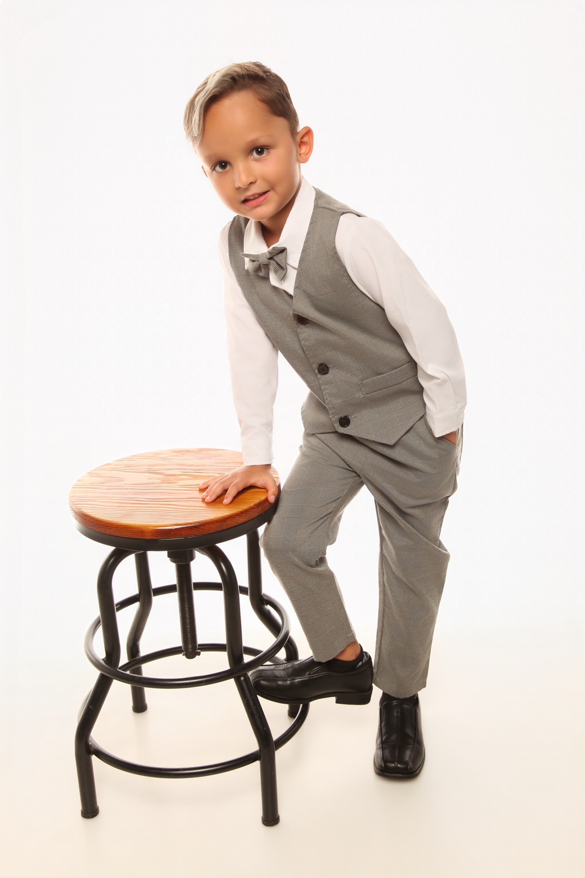 Christopher in a gray vest and bow tie, leaning on a stool